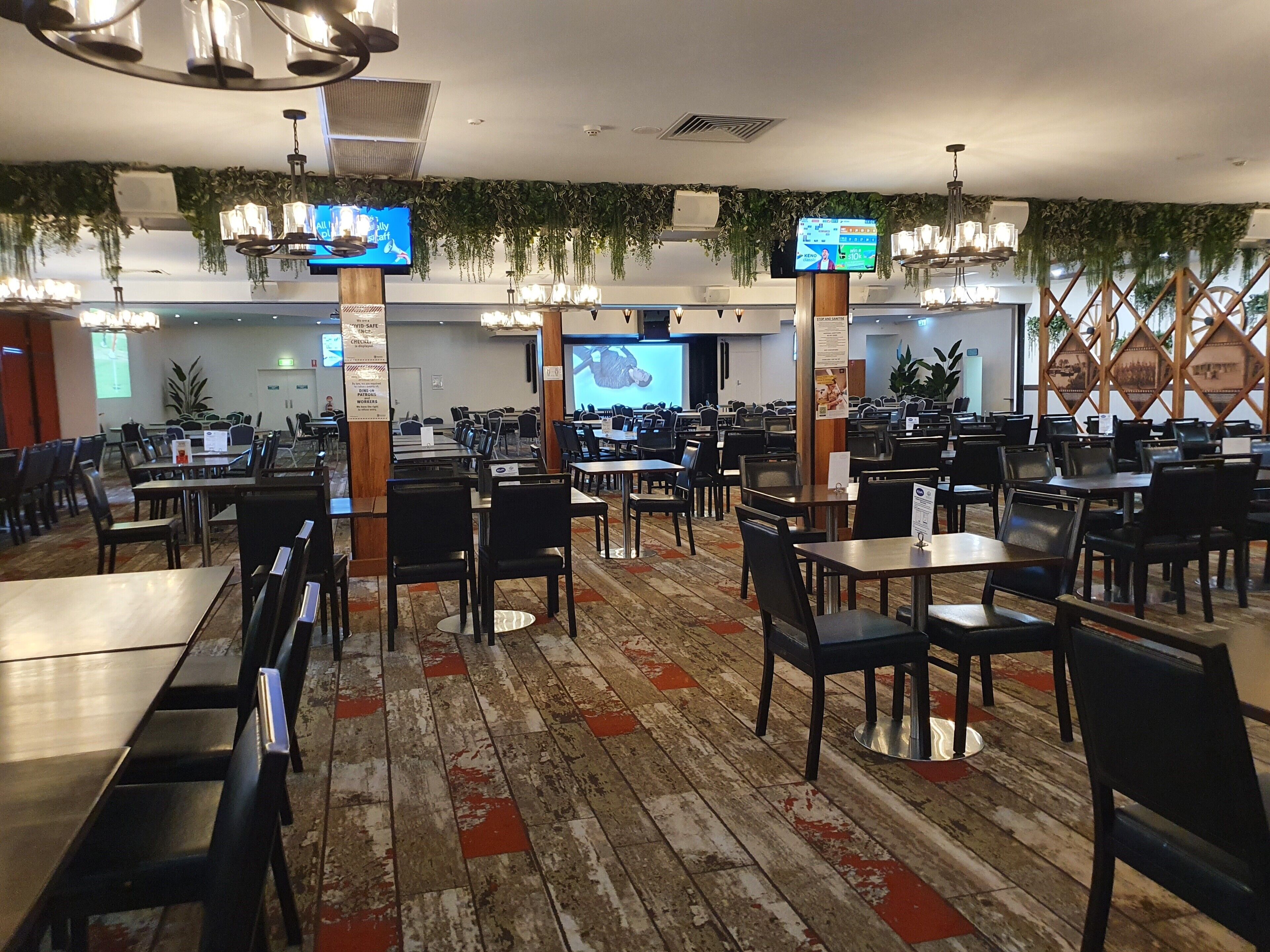 Un restaurante espacioso con múltiples mesas y sillas, ventiladores de techo y plantas colgantes.