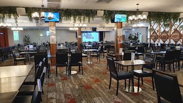 Un restaurante espacioso con múltiples mesas y sillas, ventiladores de techo y plantas colgantes.