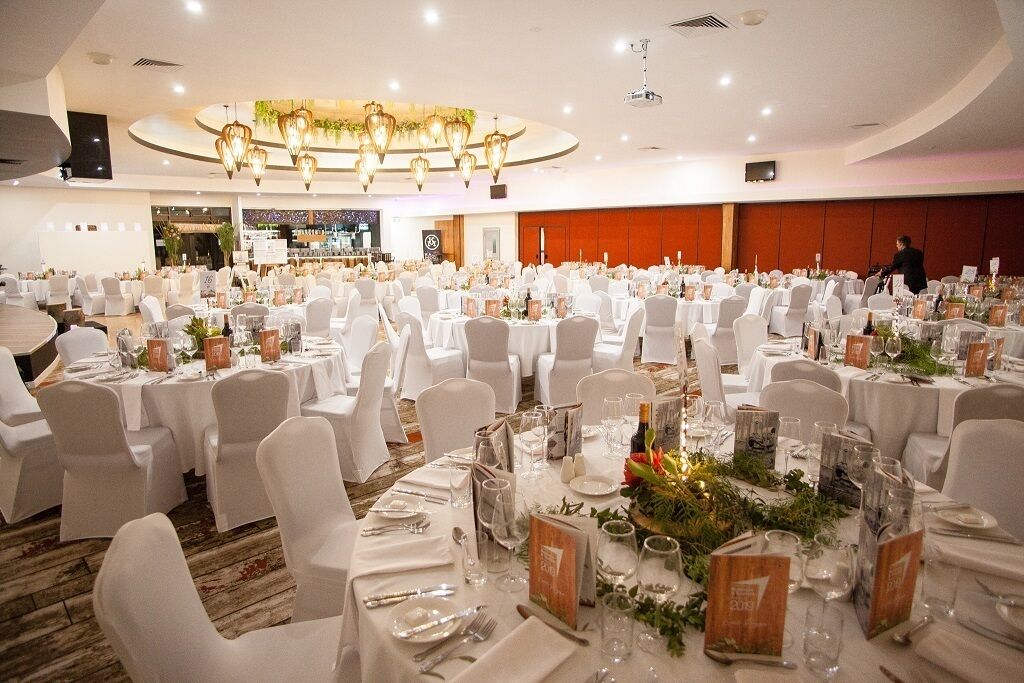 A banquet hall with round tables set for a formal event, featuring white tablecloths, chairs, and floral centerpieces.