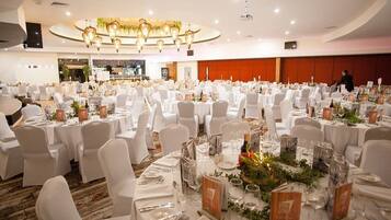 A banquet hall with round tables set for a formal event, featuring white tablecloths, chairs, and floral centerpieces.