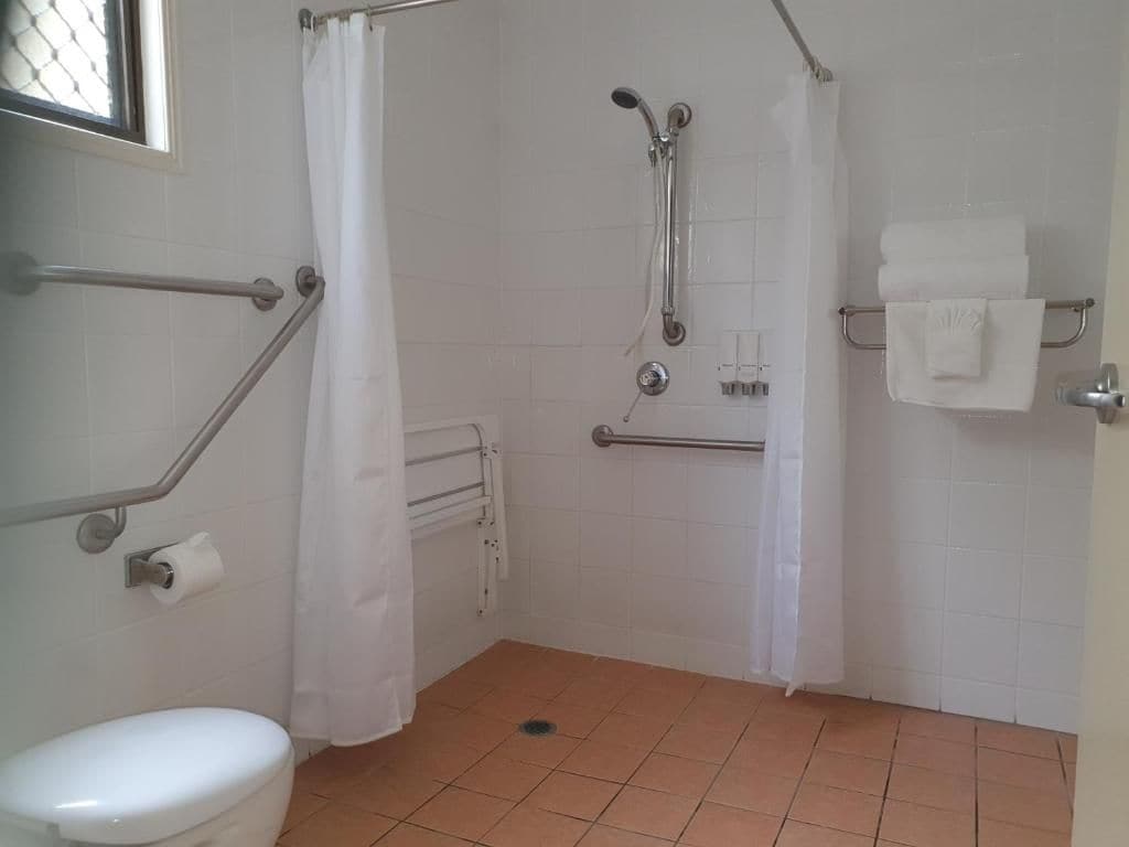 Une salle de bain équipée de toilettes, d’une douche avec des barres d’appui et d’un porte-serviettes.