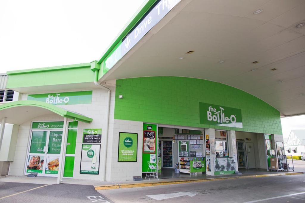 Un área de servicio con ventanilla, con una decoración en blanco y verde, un letrero que dice 'the Bottle-O' y varios anuncios.