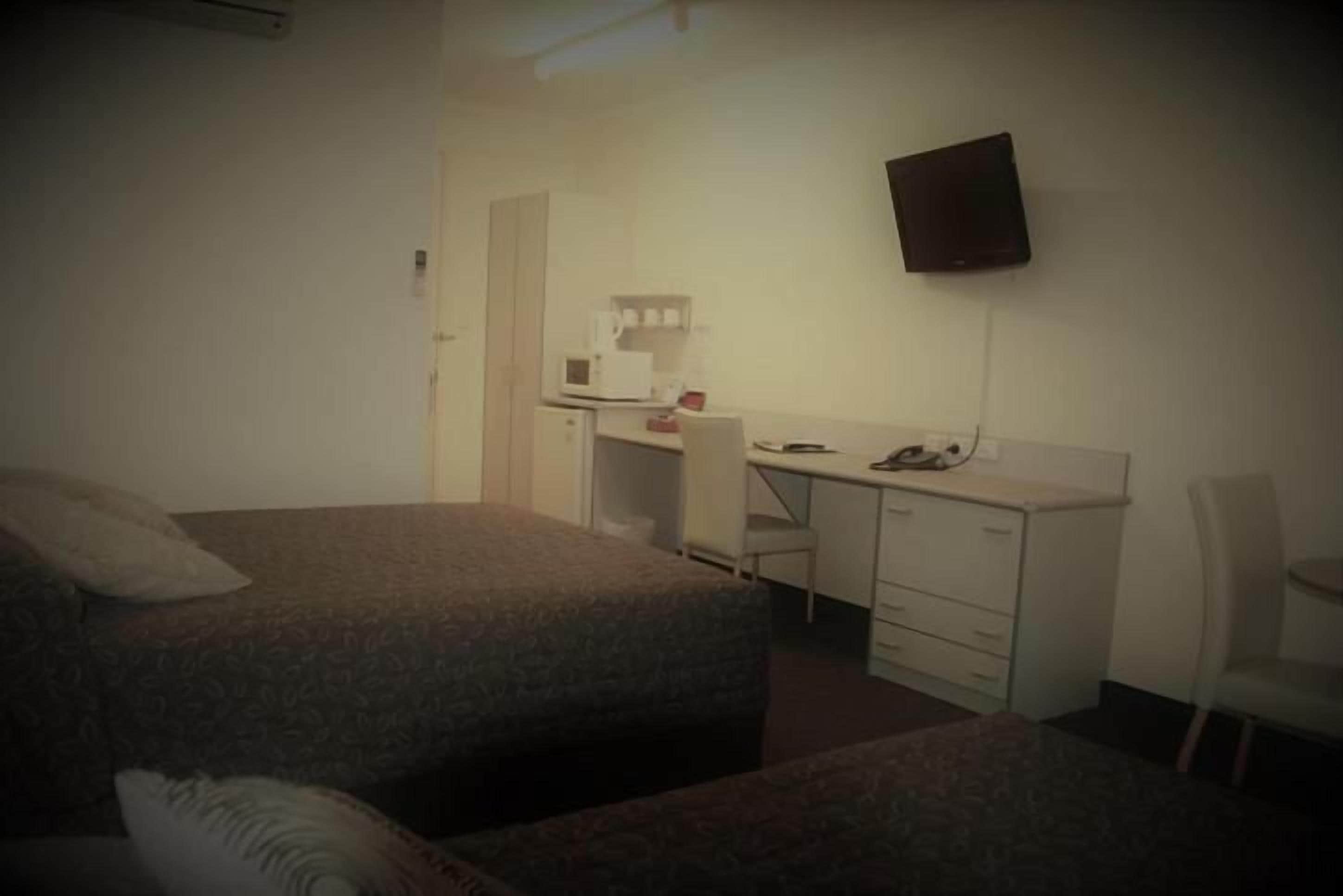 Une chambre avec deux lits, un bureau, une chaise, une télévision et un four à micro-ondes.