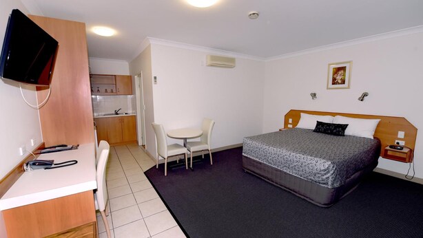 Una habitación de hotel compacta con cama, escritorio, silla, kitchenette pequeña y televisor.
