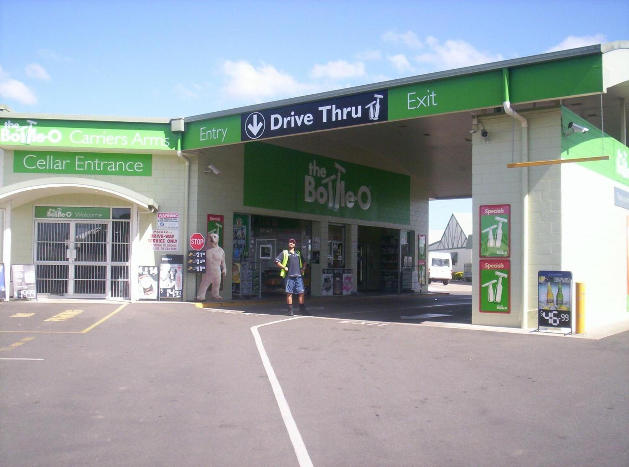 Entrada con acceso para vehículos a una tienda, con un letrero verde y una persona parada afuera.