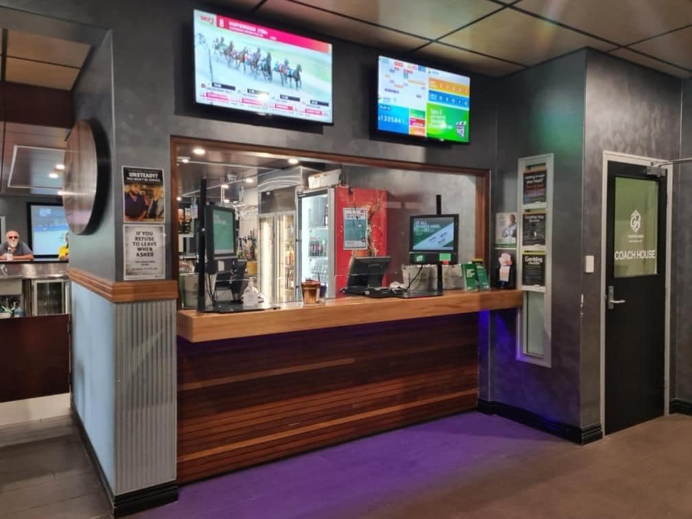 A reception desk with a wooden counter, a television screen, and a door labeled 'COACH HOUSE'.