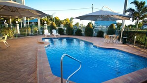 A rectangular swimming pool with a metal safety railing, surrounded by a brick patio. There are lounge chairs and umbrellas providing shade. - Carriers Arms Hotel (Maryborough)