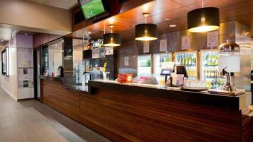 A bar area with a wooden counter, overhead TV, and various bar tools.