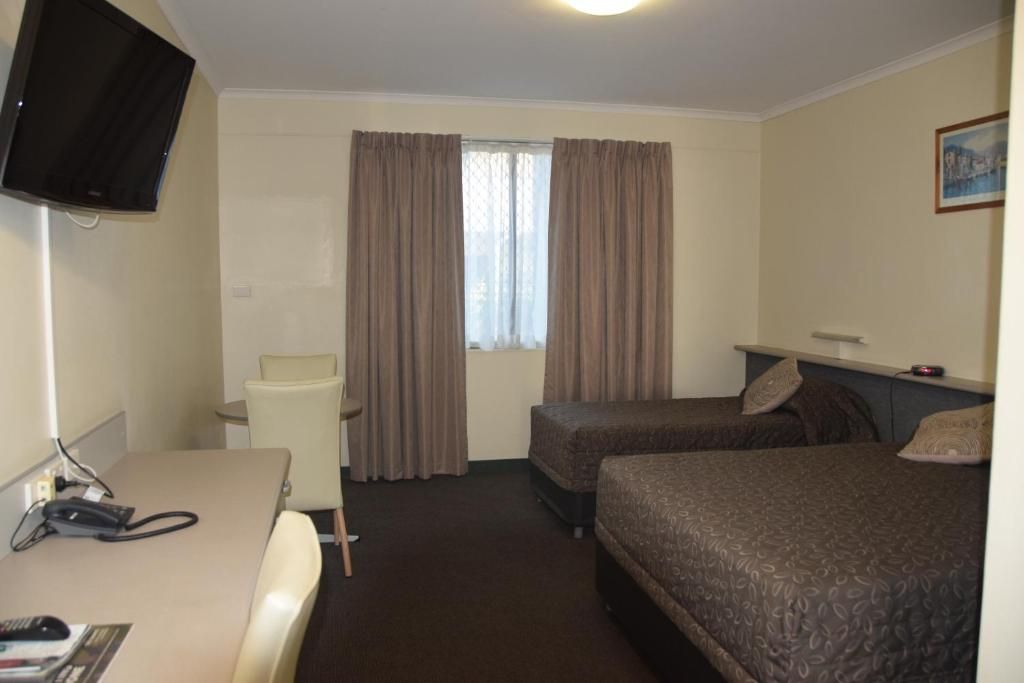 Ein Hotelzimmer mit einem Bett, einem Schreibtisch, einem Sessel, einem Fernseher und einem Fenster mit Vorhängen.