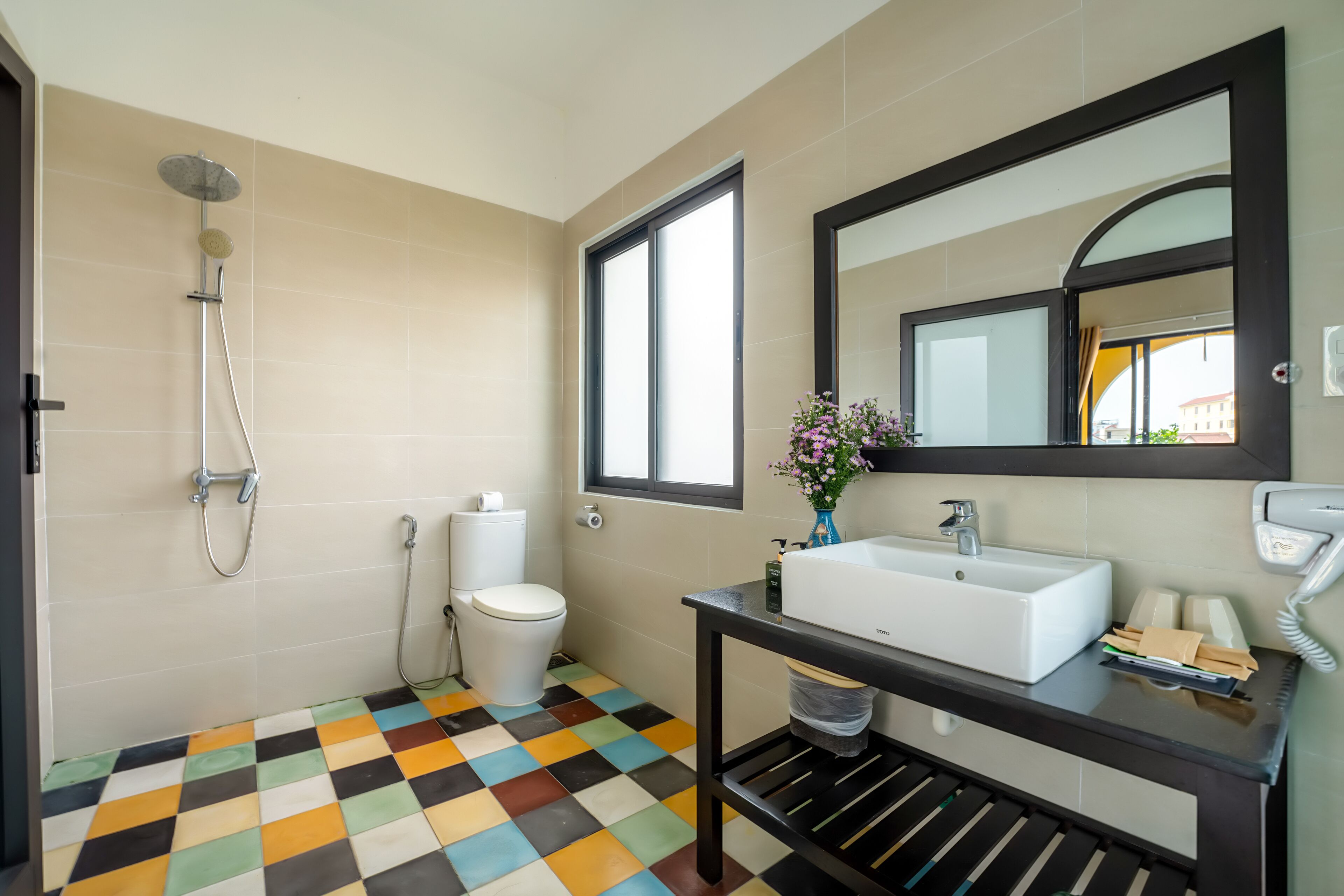 A bathroom with a checkered floor, a toilet, a shower, a sink, and a mirror.