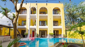 Un edificio amarillo de varios pisos con piscina, mobiliario exterior y plantas en macetas.