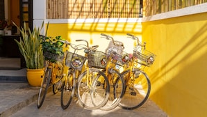 Una hilera de bicicletas amarillas estacionadas frente a un muro amarillo, con una cerca de bambú al fondo.