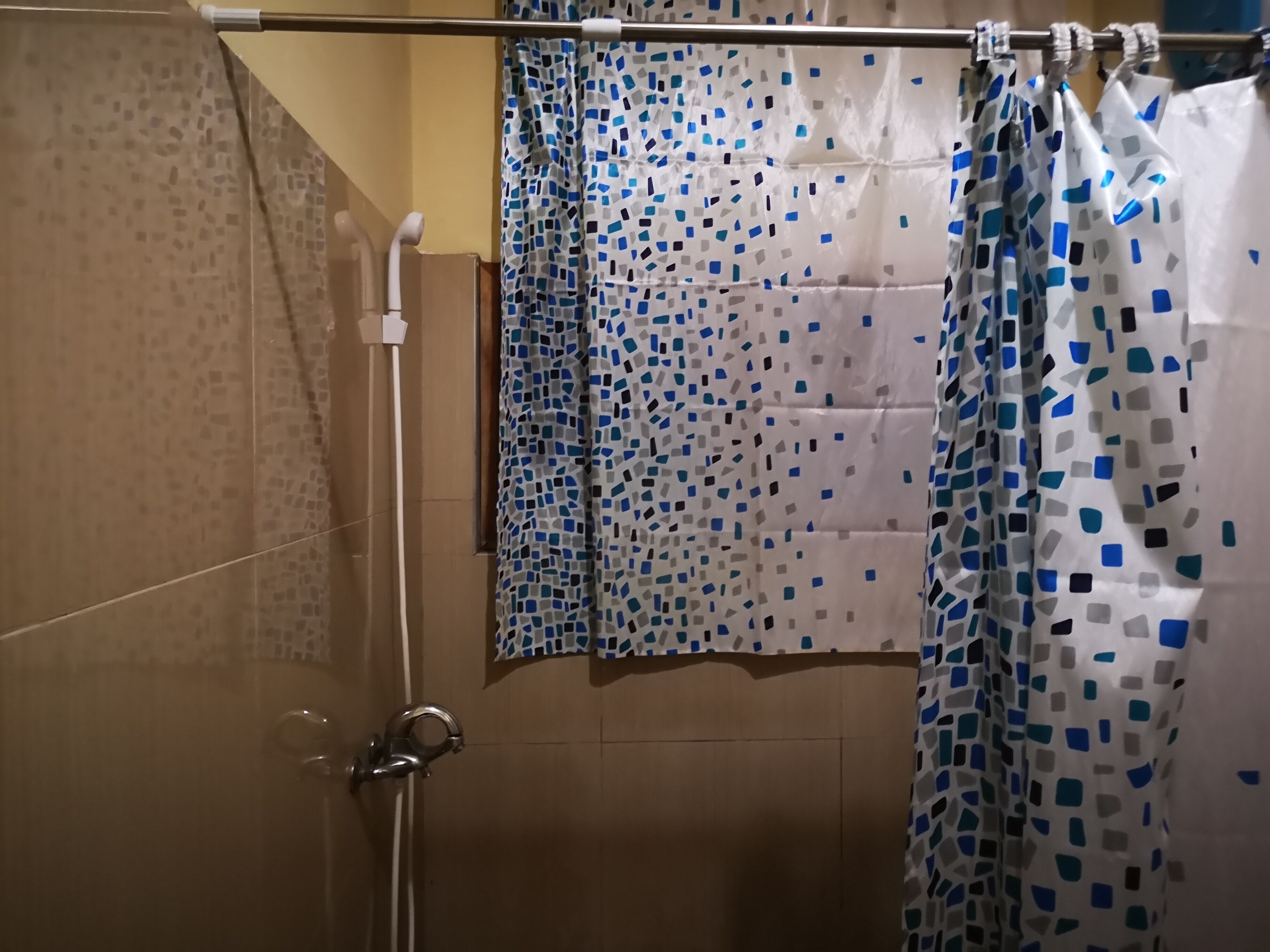 Douchegedeelte met een betegelde wand, een douchekop en een gordijn met een blauw-wit patroon.