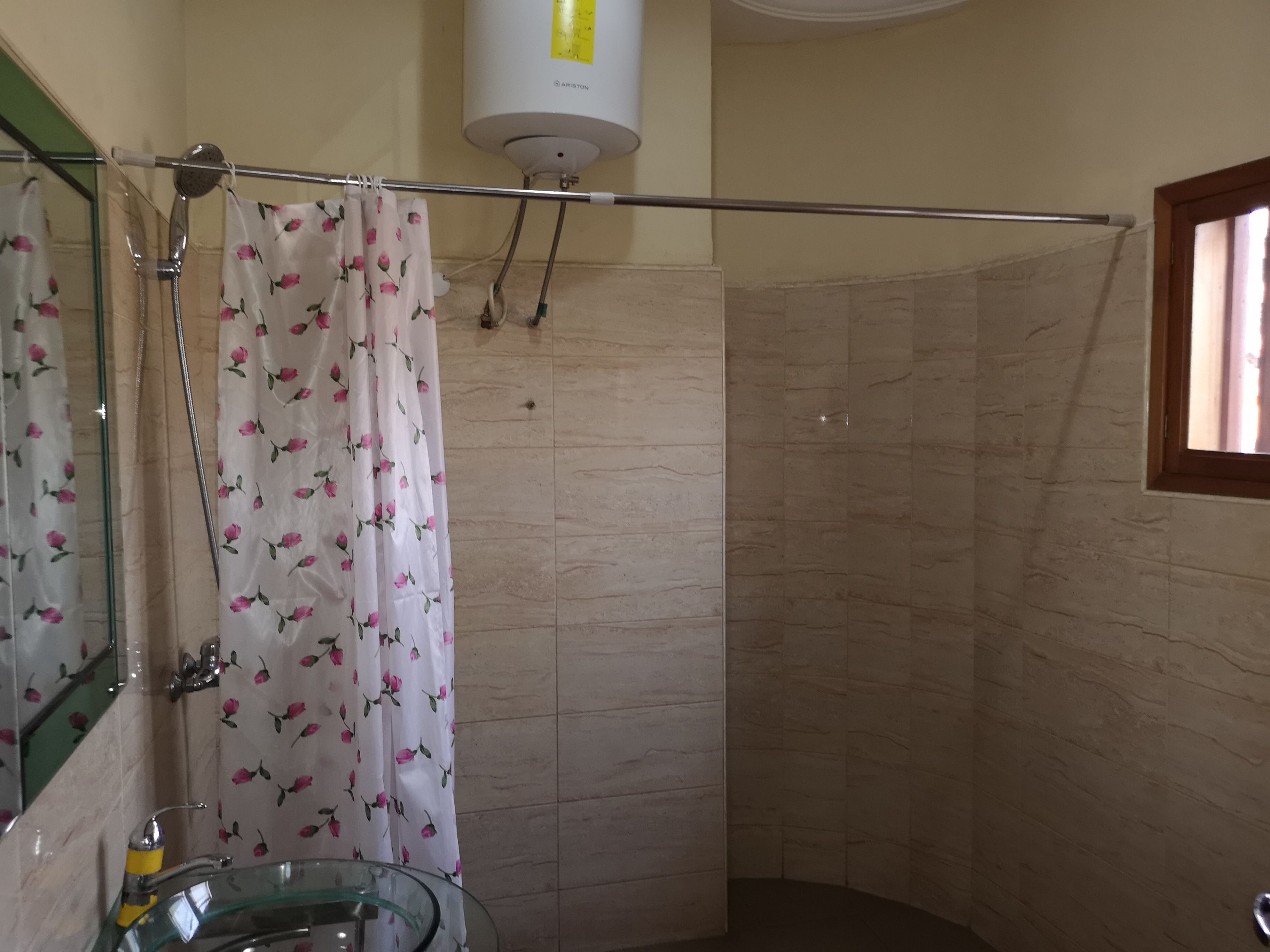 A bathroom with a glass sink, a shower with a floral curtain, and a white wall-mounted heater.