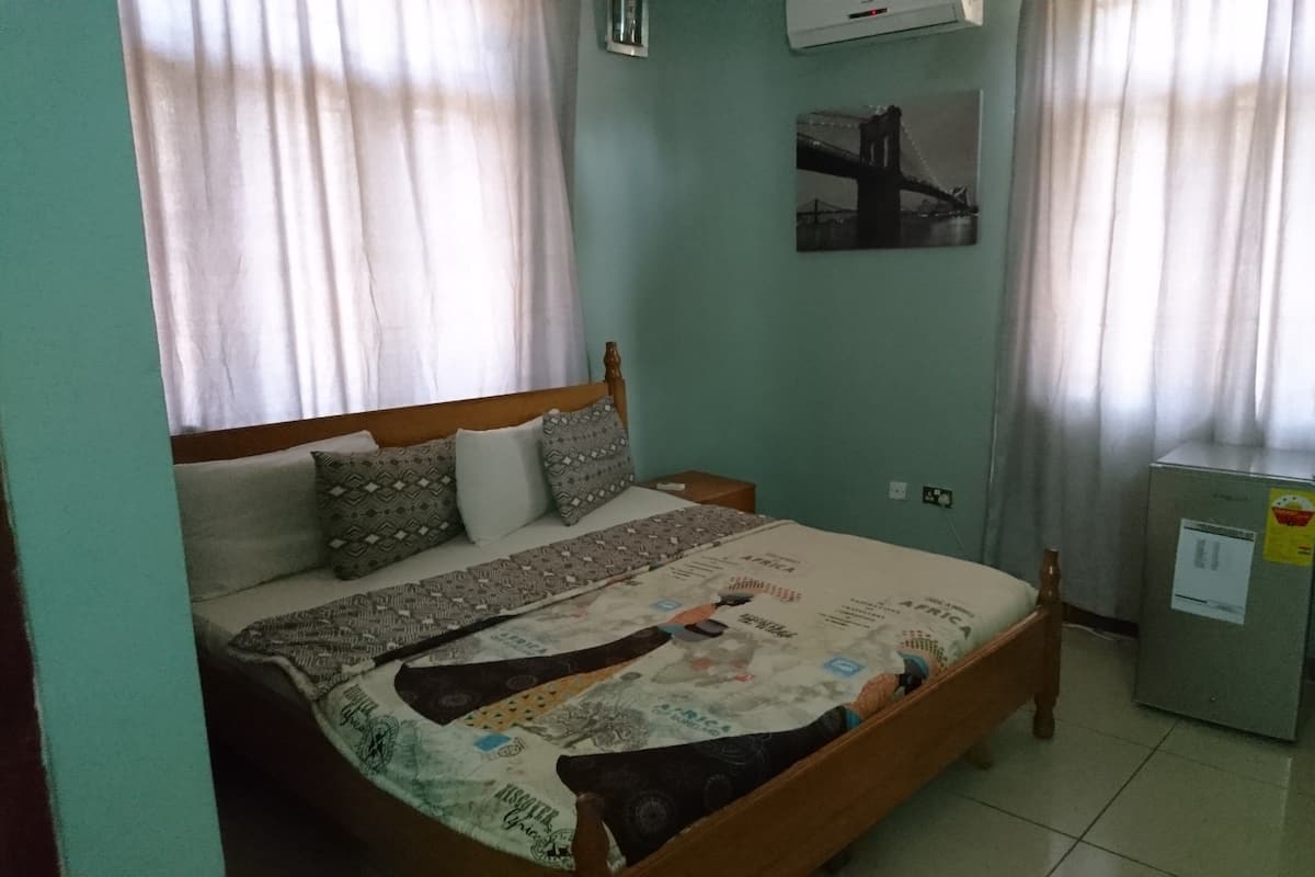 Ein Schlafzimmer mit einem Bett, Vorhängen, einem kleinen Tisch, einem Stuhl und einem Kühlschrank.