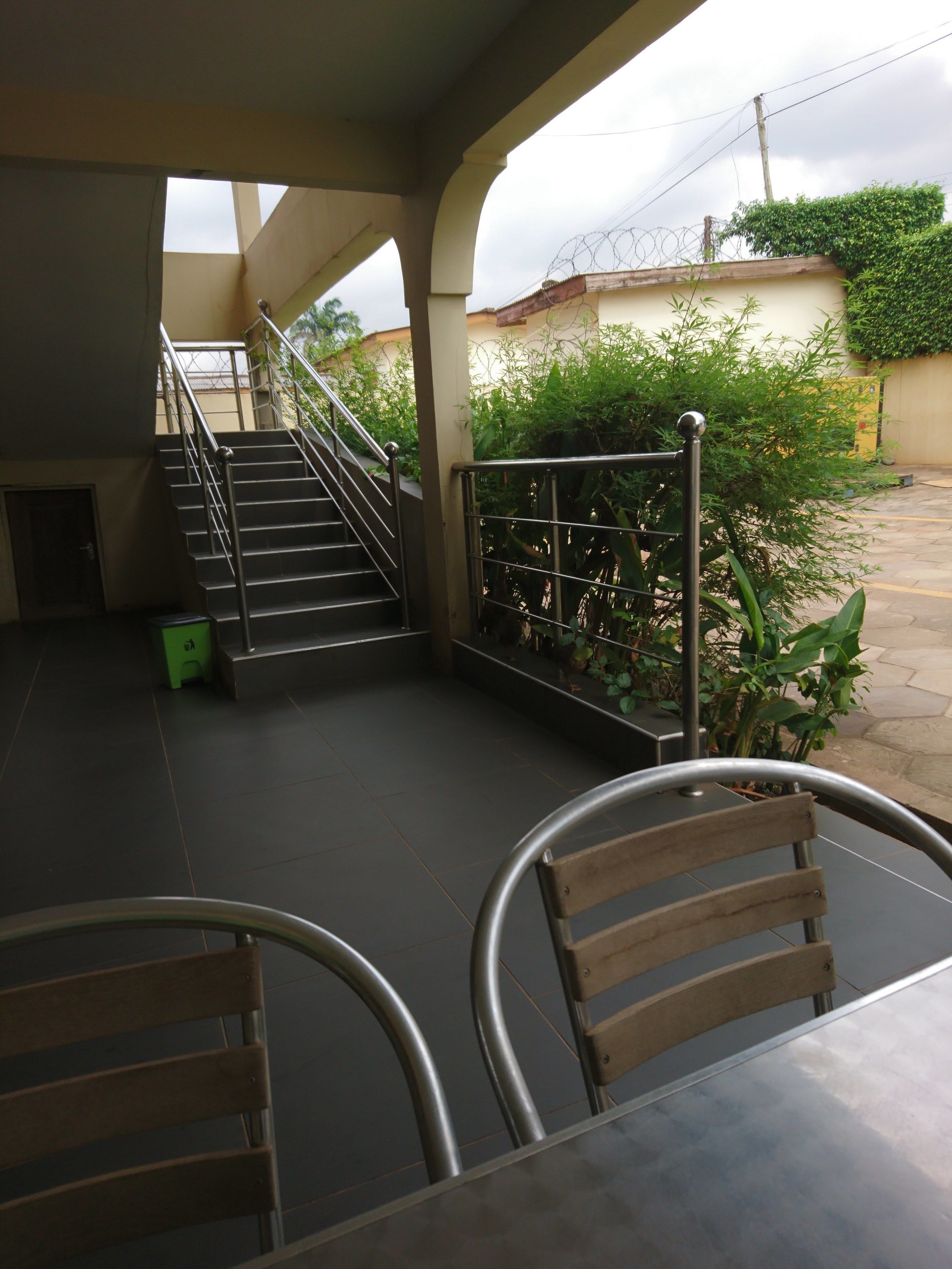 A covered outdoor area with a staircase leading to an upper level, metal railings, and a seating area with chairs.