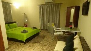 A hotel room with a bed, a small table, a sofa, a mirror, and a refrigerator.