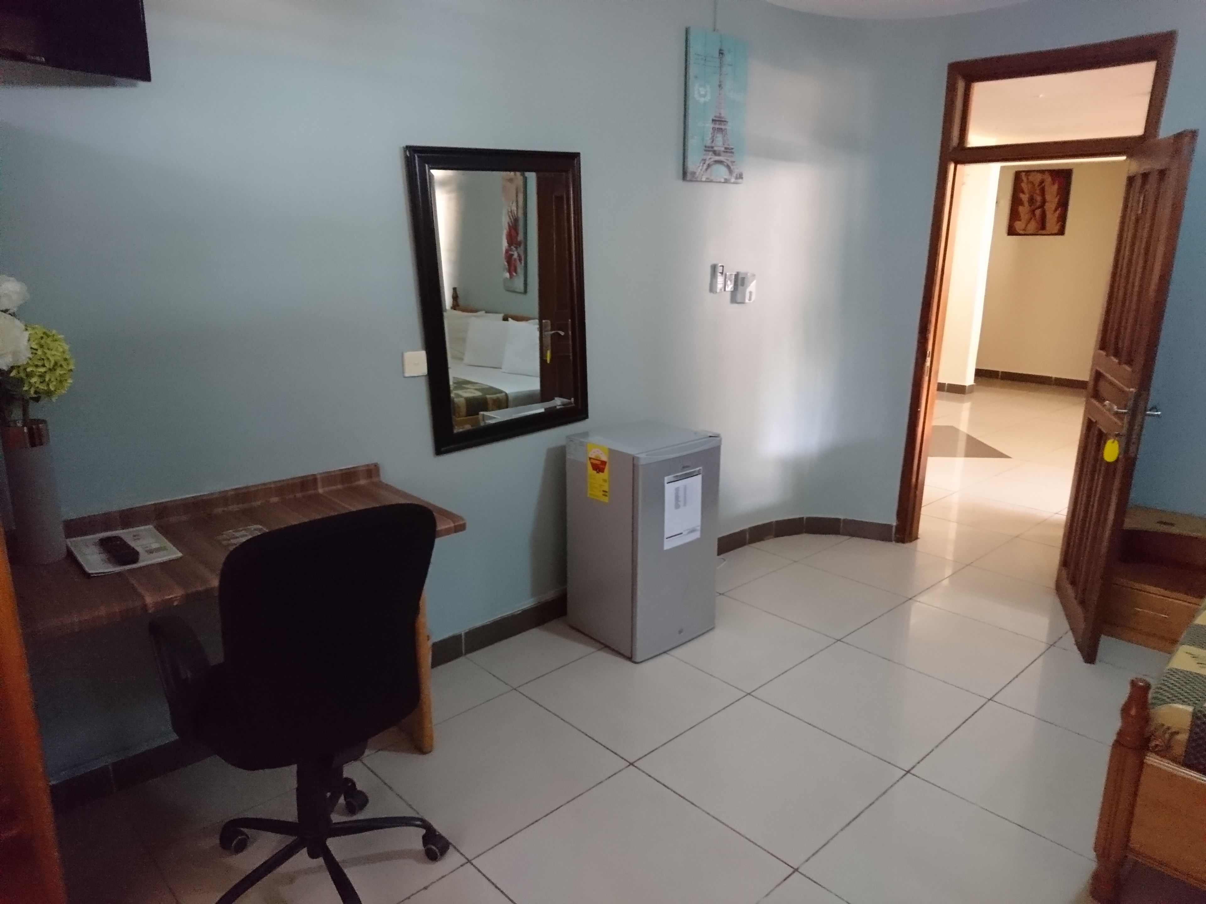 Una habitación con escritorio, silla y un refrigerador pequeño.
