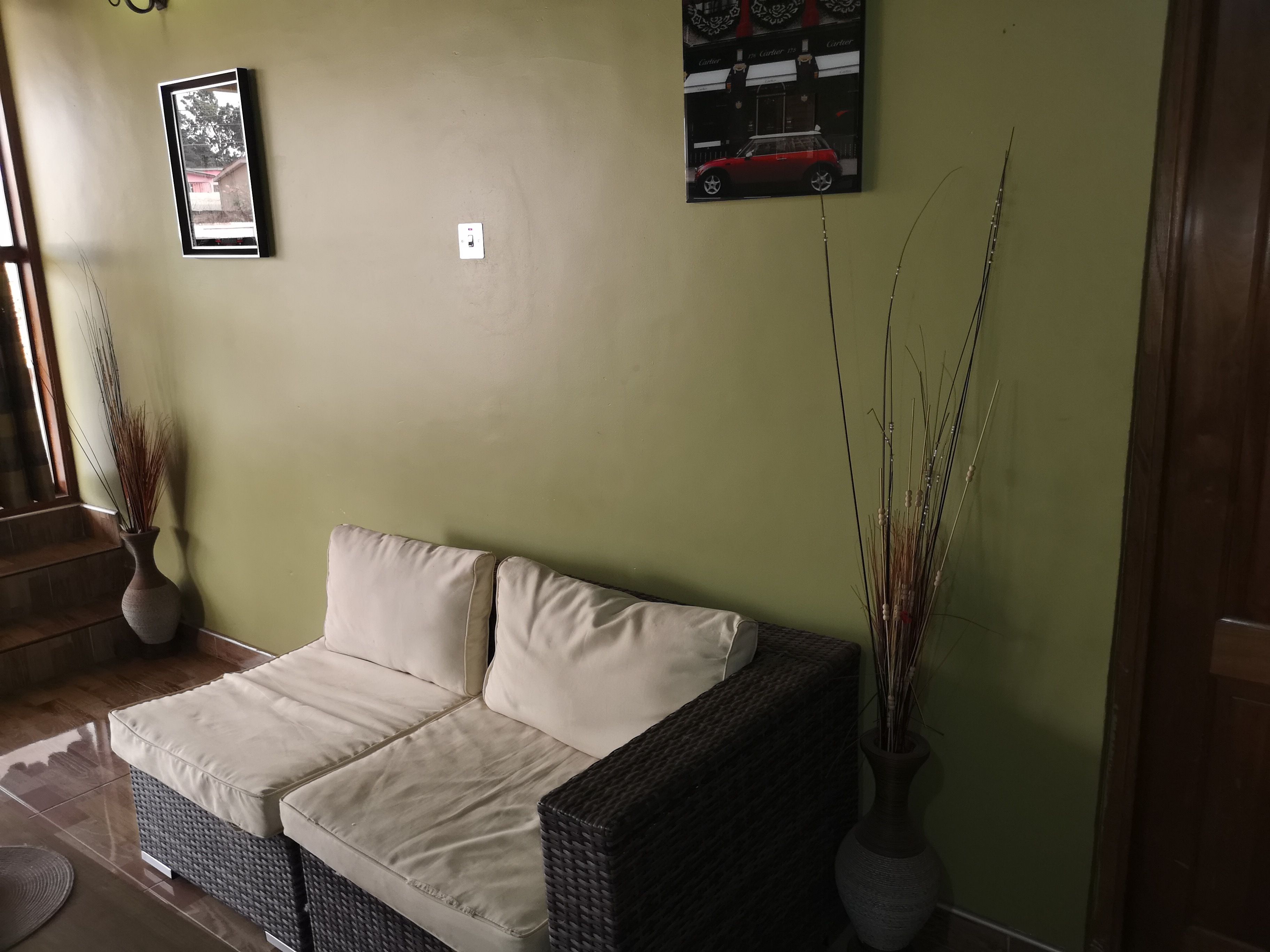 Una habitación con un sofá color beige, dos jarrones con plantas altas y dos cuadros en la pared.