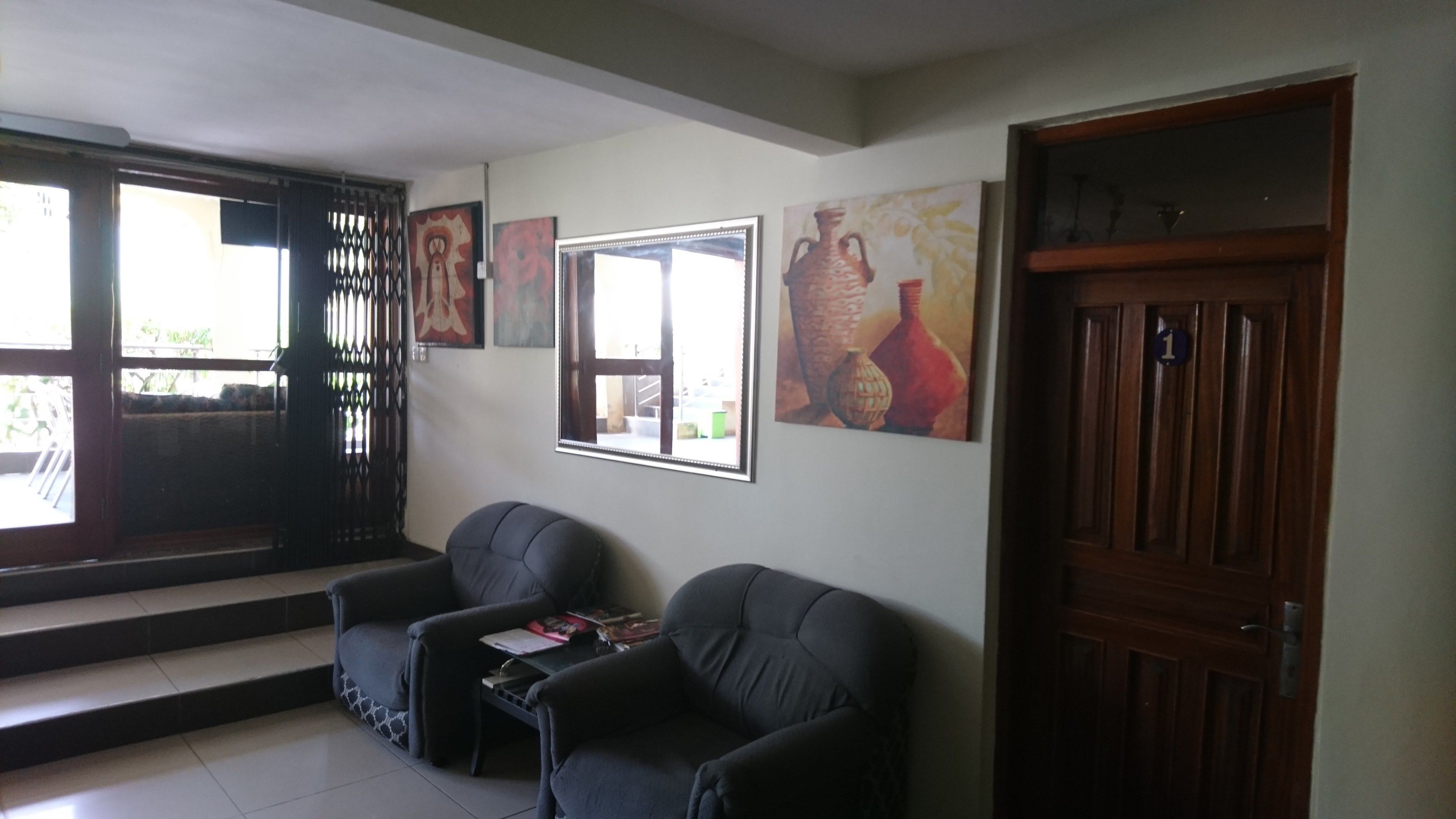 Ein Zimmer mit zwei schwarzen Sofas, einem kleinen Tisch und einer Holztür. An der Wand hängen drei gerahmte Kunstwerke.