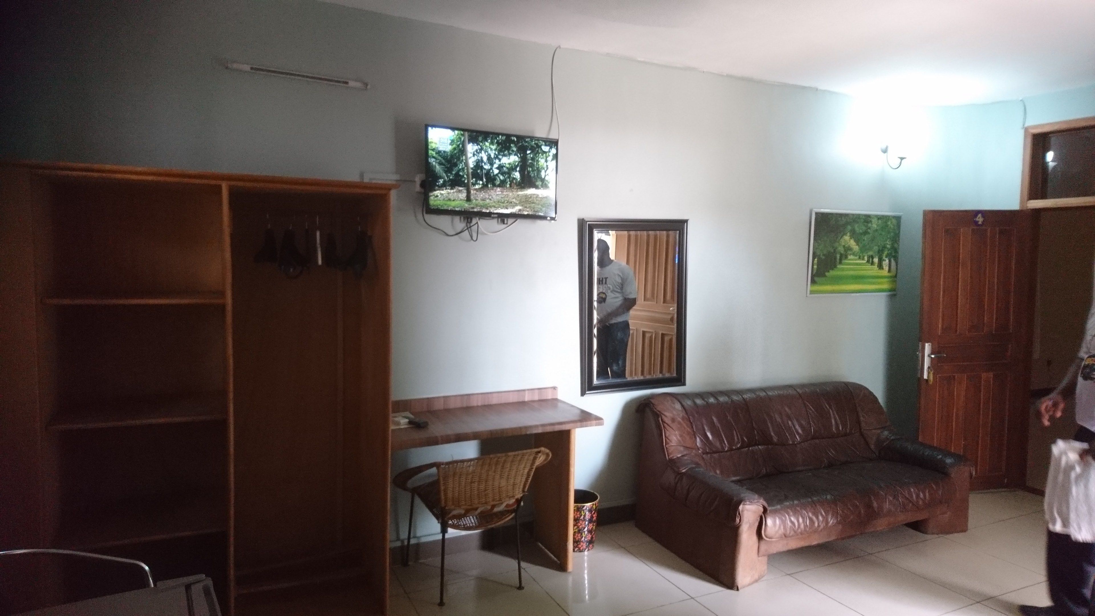 A living room with a brown leather sofa, a wooden desk, a television mounted on the wall, and a door.