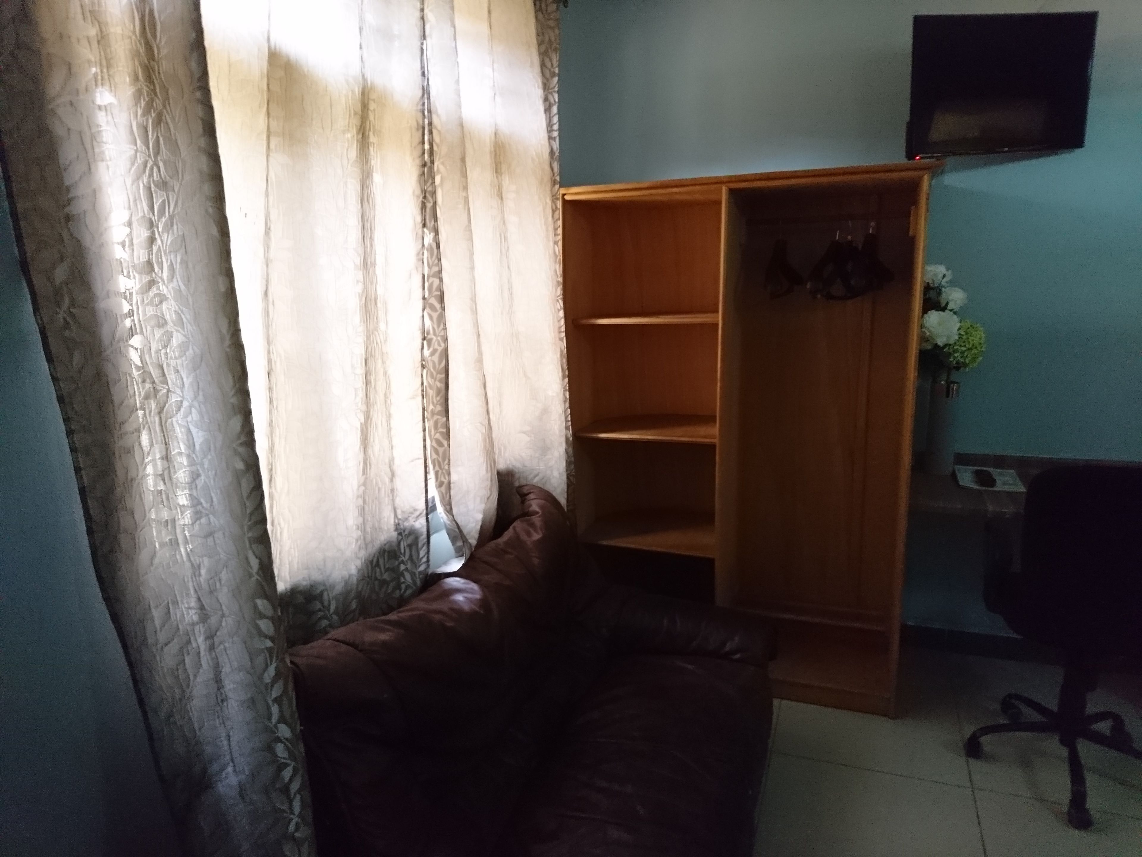 Una habitación con un sofá de cuero marrón, un armario de madera y un televisor en la pared.