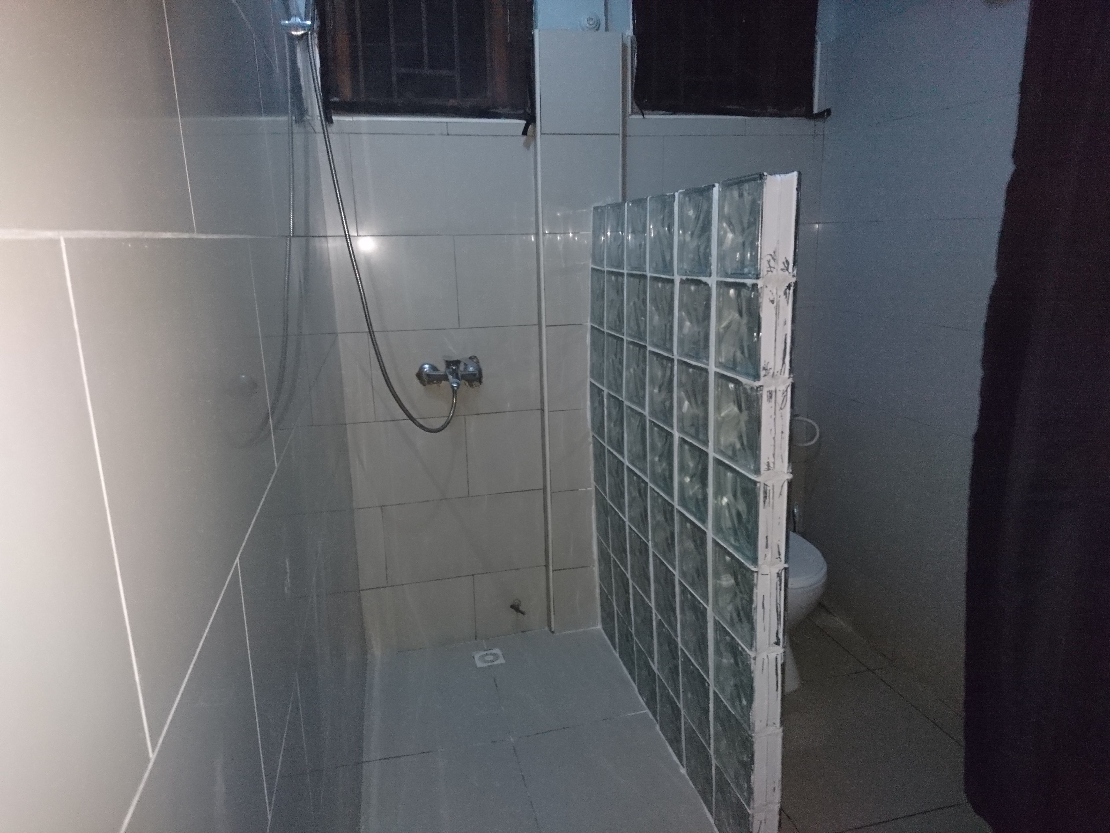 A small, tiled bathroom with a shower, a toilet, and a glass partition.