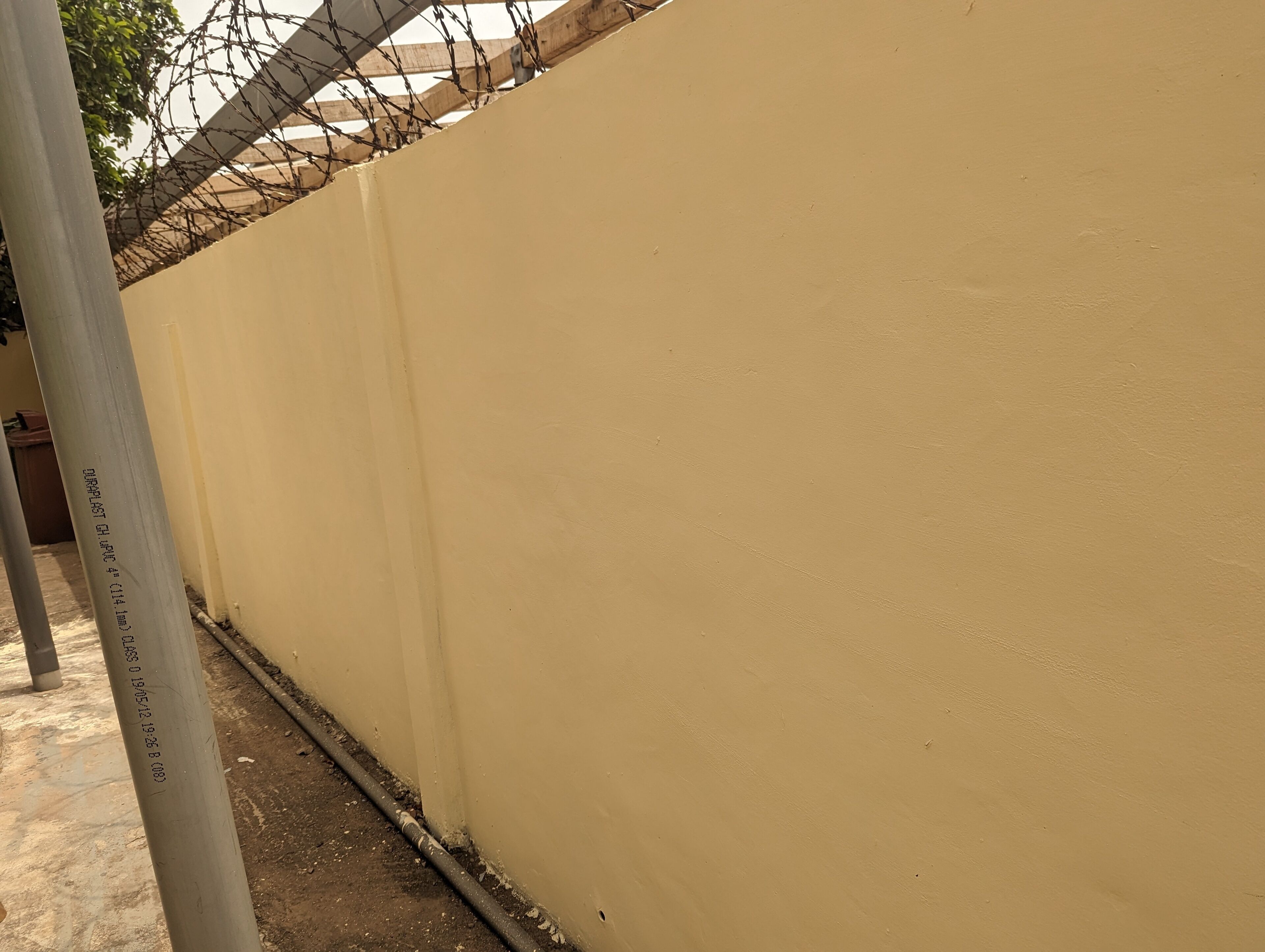 Eine beige Wand mit einem Stacheldrahtzaun darauf.