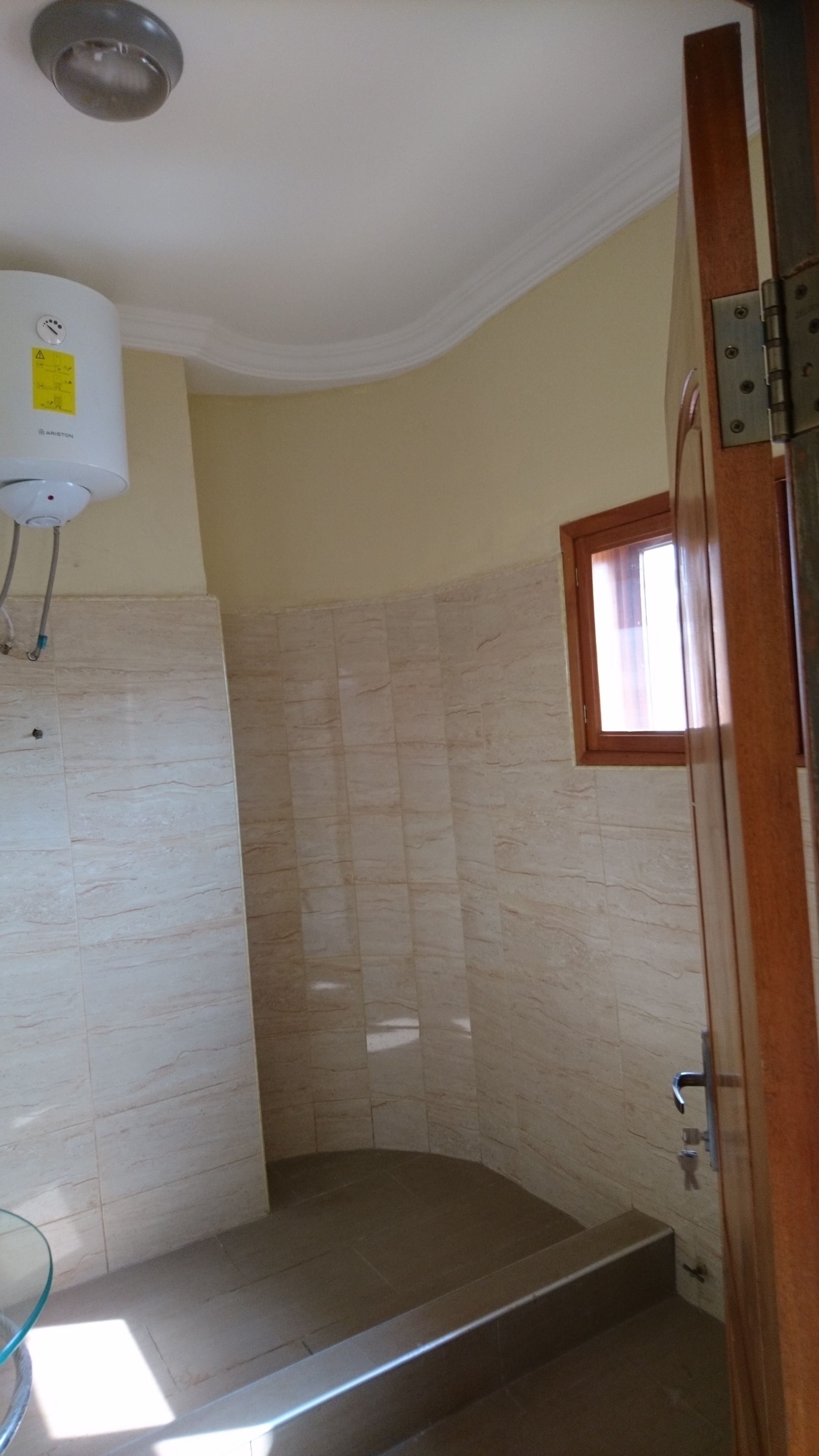A bathroom with a shower, tiled walls, a window, and a water heater.