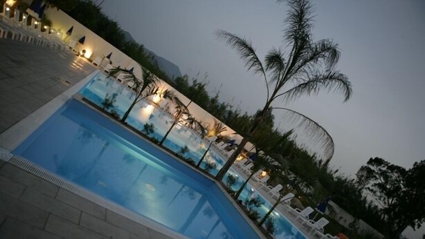 A swimming pool with lounge chairs and palm trees, surrounded by a tiled walkway. - Batuca Village & Camping (Terme Vigliatore)