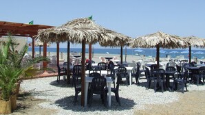 An outdoor seating area with tables and chairs, thatched umbrellas, and a view of the beach and sea. - Batuca Village & Camping (Terme Vigliatore)