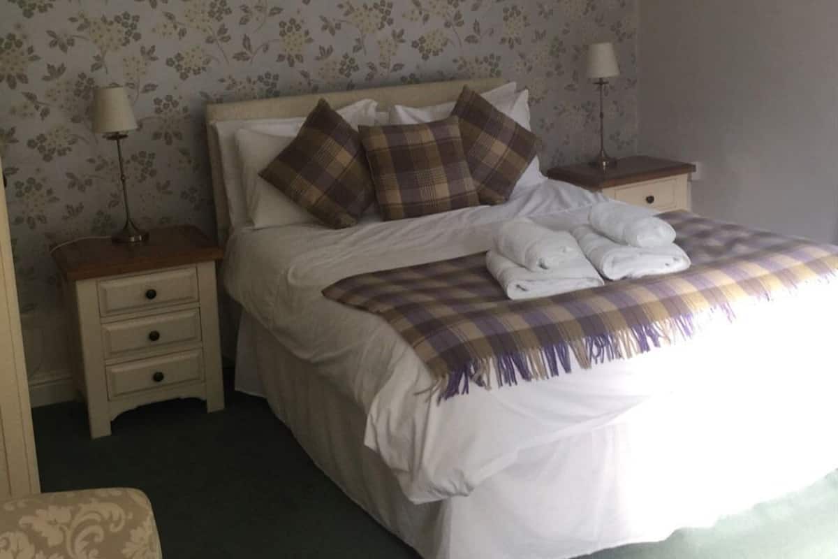 A neatly made bed with a plaid blanket and pillows, a bedside lamp, and a nightstand with drawers.