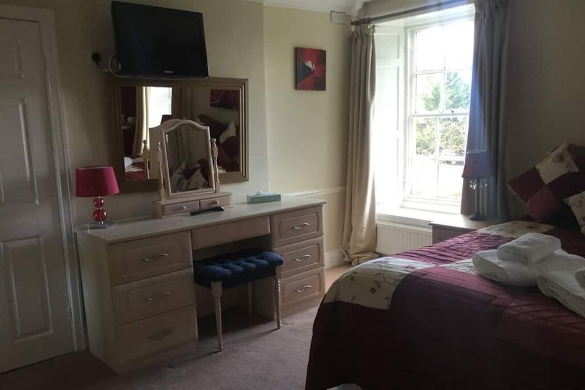 A bedroom with a bed, a dresser, a mirror, a television, and a window with curtains.