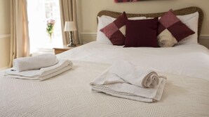 A neatly made bed with white linens and a patterned duvet, a nightstand with a lamp, and a painting of a rose on the wall. - The Coachman Inn (Scarborough)