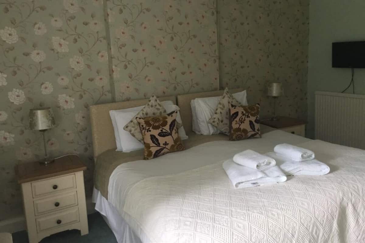 A neatly made bed with floral-patterned pillows, a bedside lamp, and folded towels on a nightstand.