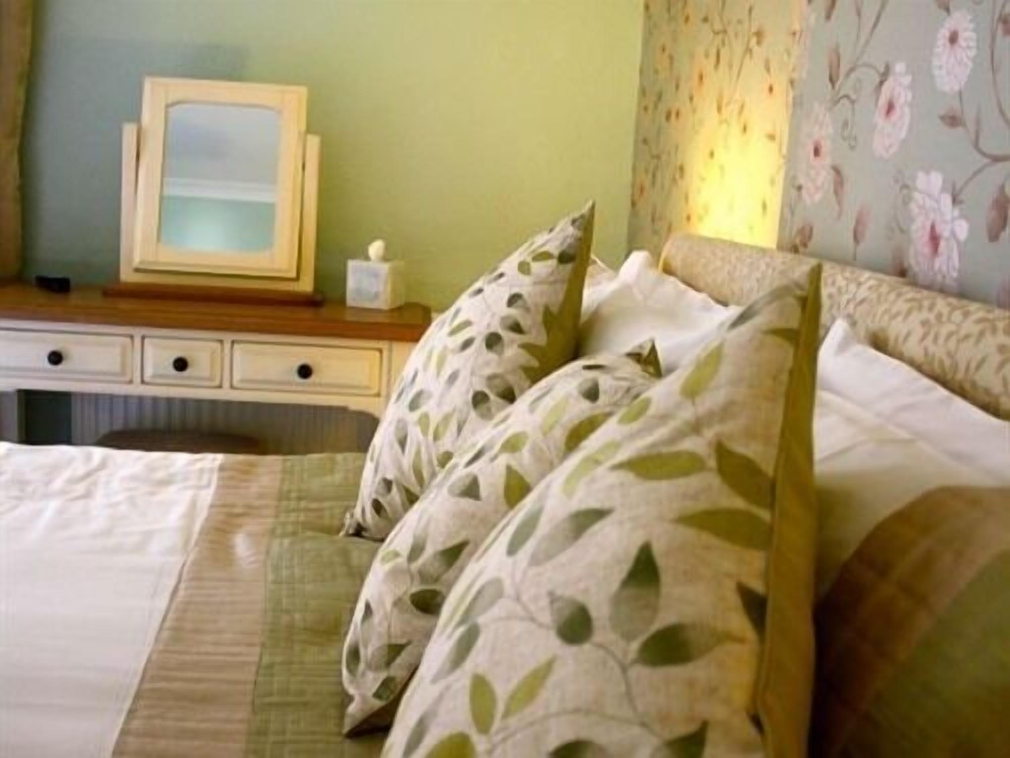 Una cama bien hecha con almohadones estampados con motivos florales y un cabecero de madera.