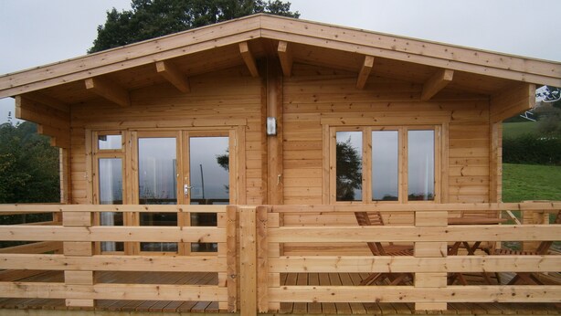 A wooden cabin with a balcony, large windows, and a wooden deck. - Long Mountain Centre (Shrewsbury)