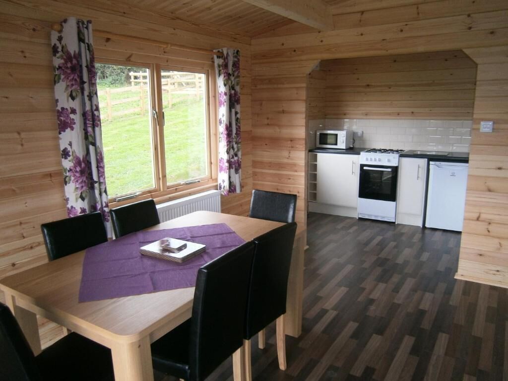 A wooden interior with a dining table, chairs, a kitchen area with appliances, and a view of the outdoors.