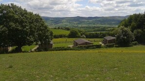 A rural landscape with rolling hills, a large tree, and two wooden buildings. - Long Mountain Centre (Shrewsbury)