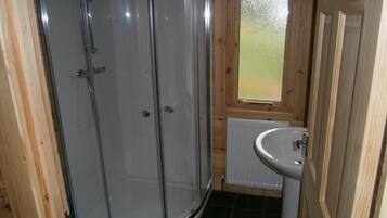 Un baño con cabina de ducha de vidrio, inodoro, lavamanos y ventana.