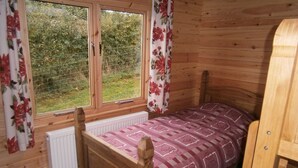 A wooden room with a bed, a window with curtains, and a radiator. - Long Mountain Centre (Shrewsbury)