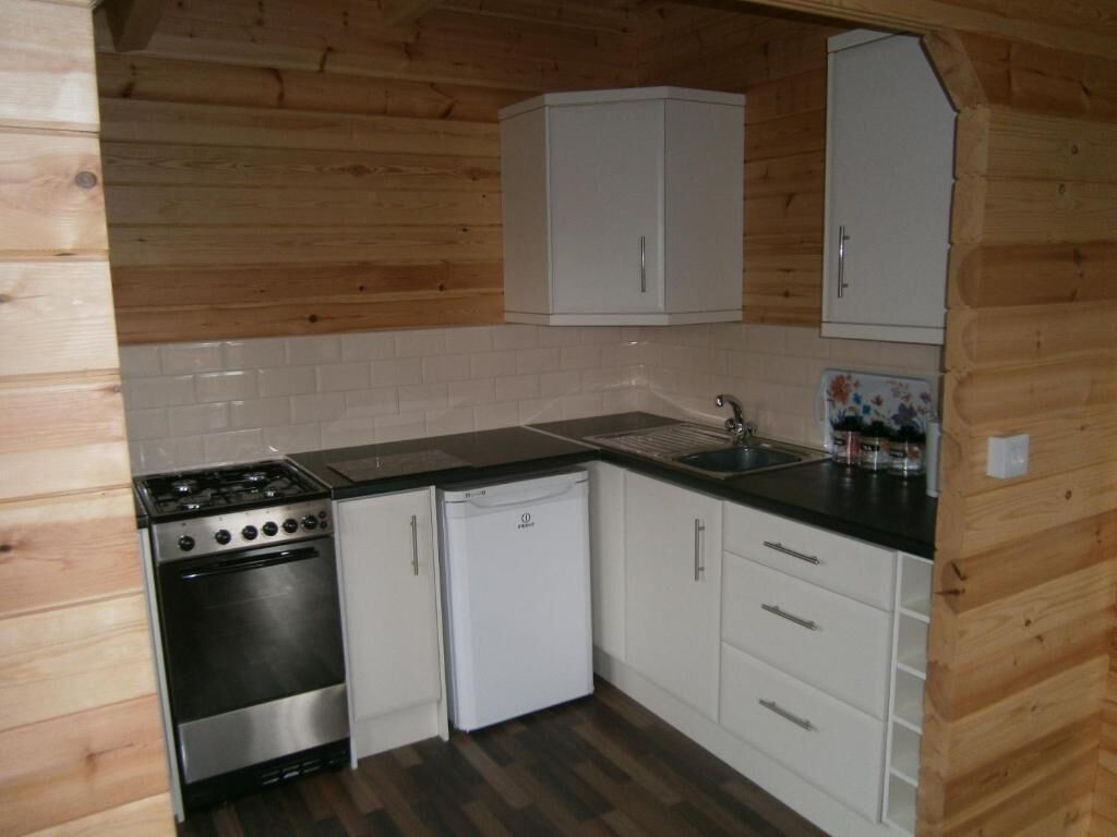 A compact kitchen with a stove, oven, and dishwasher, wooden walls, and white cabinets.