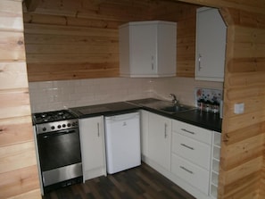 A compact kitchen with a stove, oven, and dishwasher, wooden walls, and white cabinets. - Long Mountain Centre (Shrewsbury)