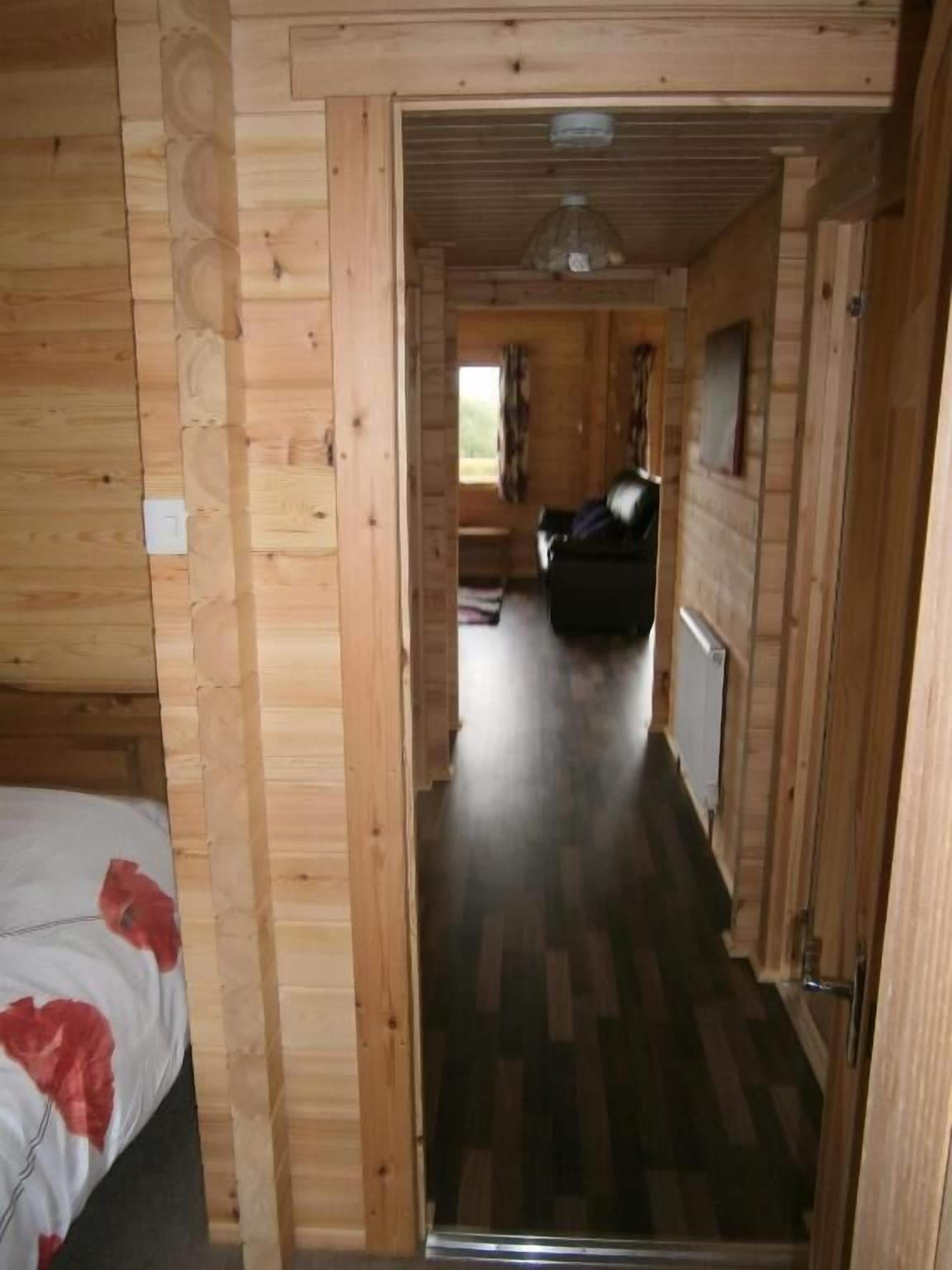 A wooden interior with a bed, a door leading to another room, and a window.