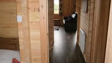 A wooden interior with a bed, a door leading to another room, and a window.