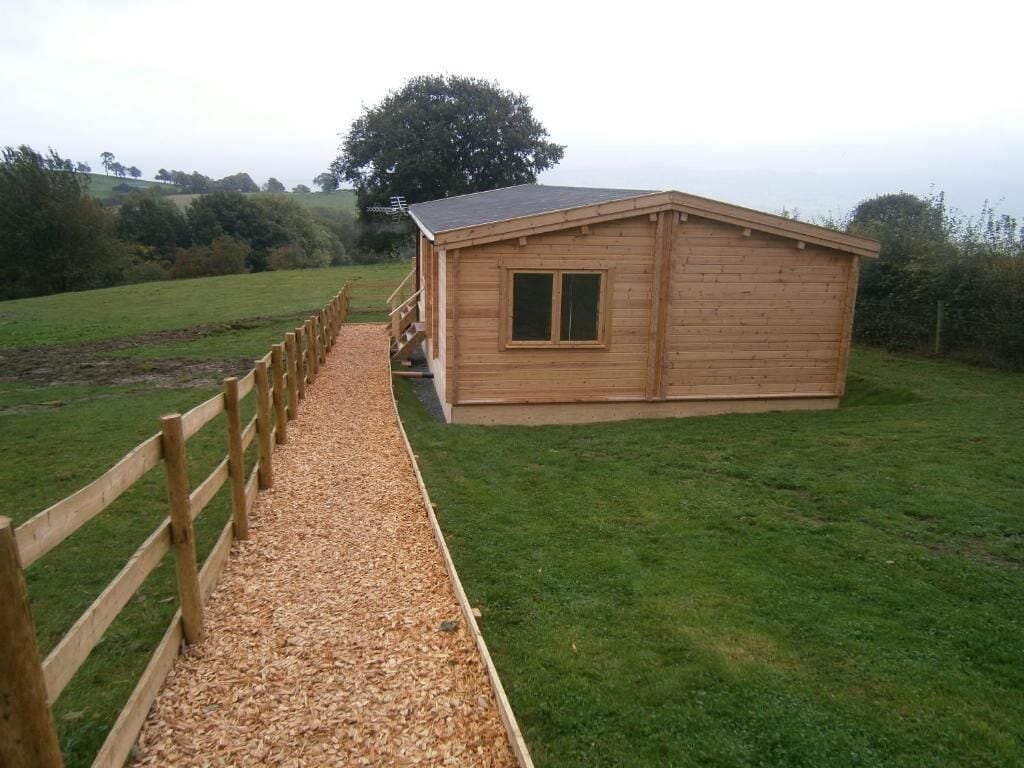 A wooden building with a sloped roof, a wooden fence, and a gravel path leading to it.