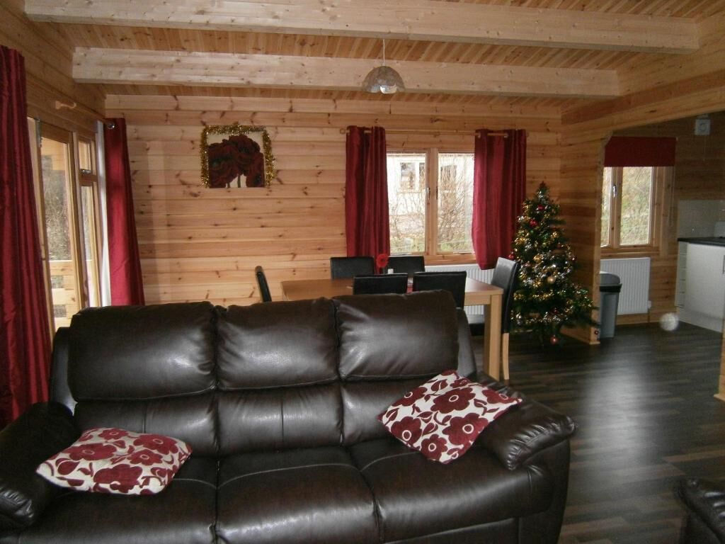 A wooden interior with a leather sofa, a dining table, and a Christmas tree.