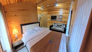 Et hyggeligt sommerhusværelse med seng, sofa, fjernsyn og lampe.