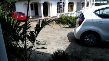 A building with a white facade, a red car parked in front, and a white car parked to the right.