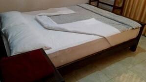 A neatly made bed with a white comforter and pillows, a wooden headboard, and a red pillow on the floor. - Amaya View Guest Inn (Haputhale)